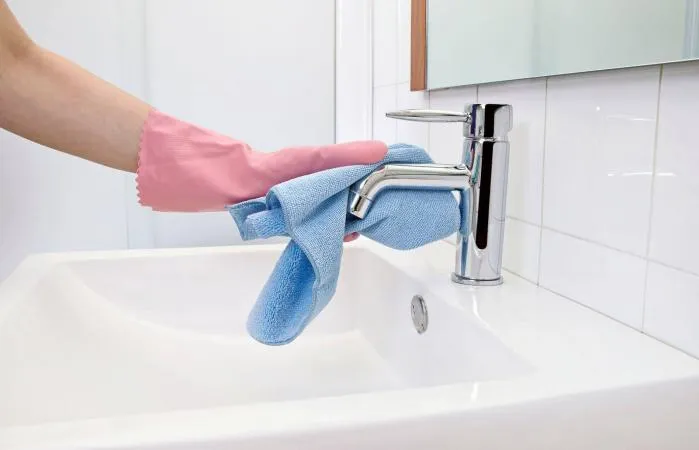 A professional cleaner wipes down a chrome faucet, ensuring it shines and is spotless.