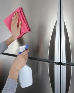 a cleaning spray and cloth to wipe down a stainless steel refrigerator during an end-of-lease clean."