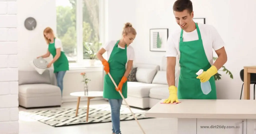 A team of cleaners in green aprons working in a bright home.