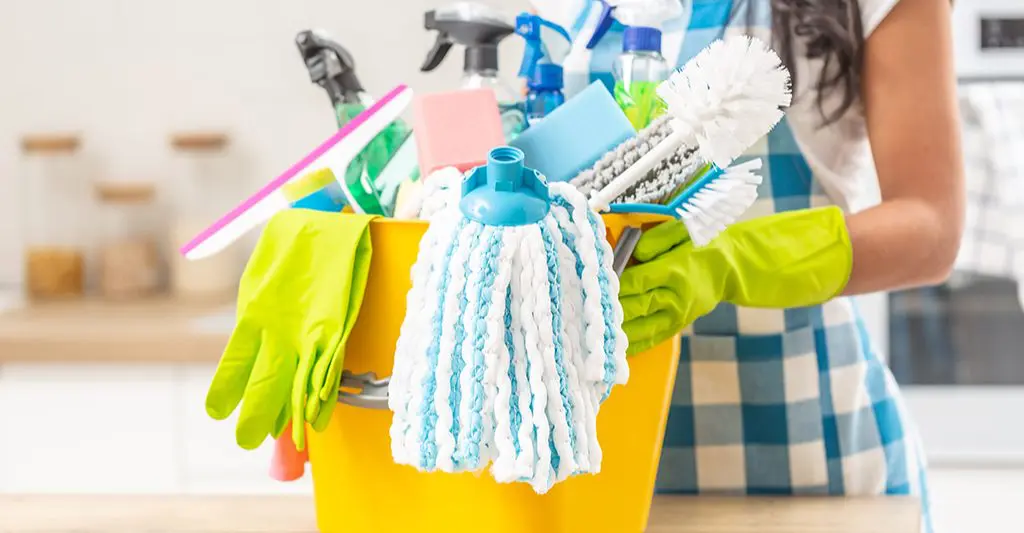 How to choose the best end of lease cleaning company? 2 A yellow bucket filled with cleaning supplies held by a person wearing green gloves.