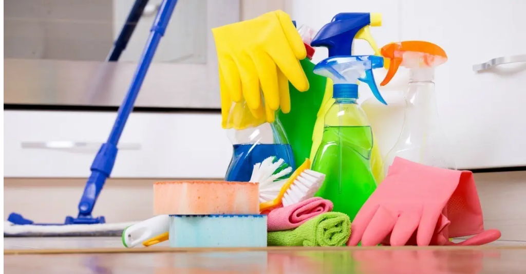 How to choose the best end of lease cleaning company? 3 Various cleaning supplies and gloves arranged on the floor in front of a kitchen cabinet.