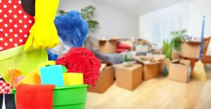 A person holding a green cleaning kit in front of a room filled with cardboard moving boxes.