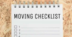 A spiral notebook titled "Moving Checklist" with empty checkboxes placed on a wooden surface.