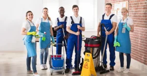 A smiling group of professional cleaners standing with cleaning tools and equipment, ready for service.