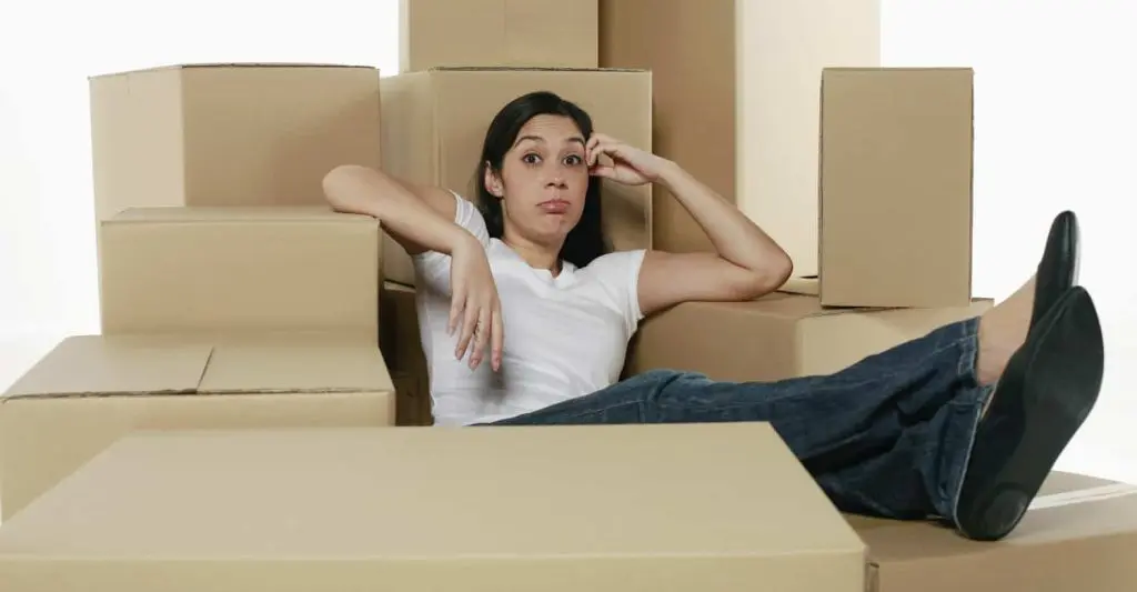A woman looks exhausted while sitting among several cardboard boxes during a house move.
