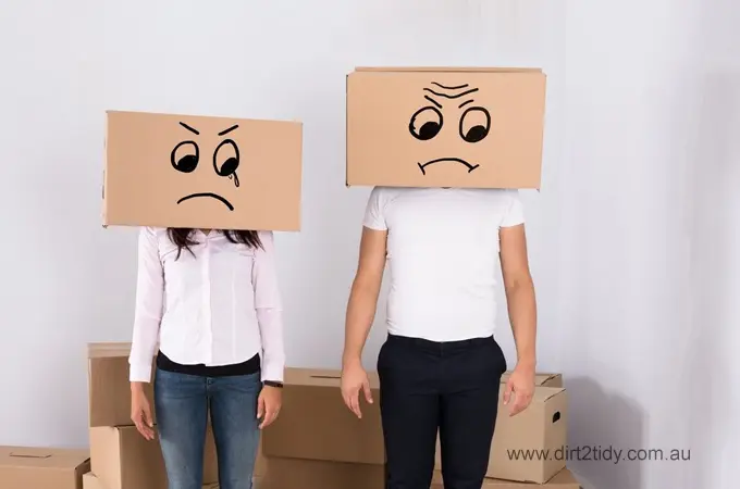 Unhappy couple with cardboard boxes on their heads showing sad faces – representing the stress of moving out without help from professional cleaners.