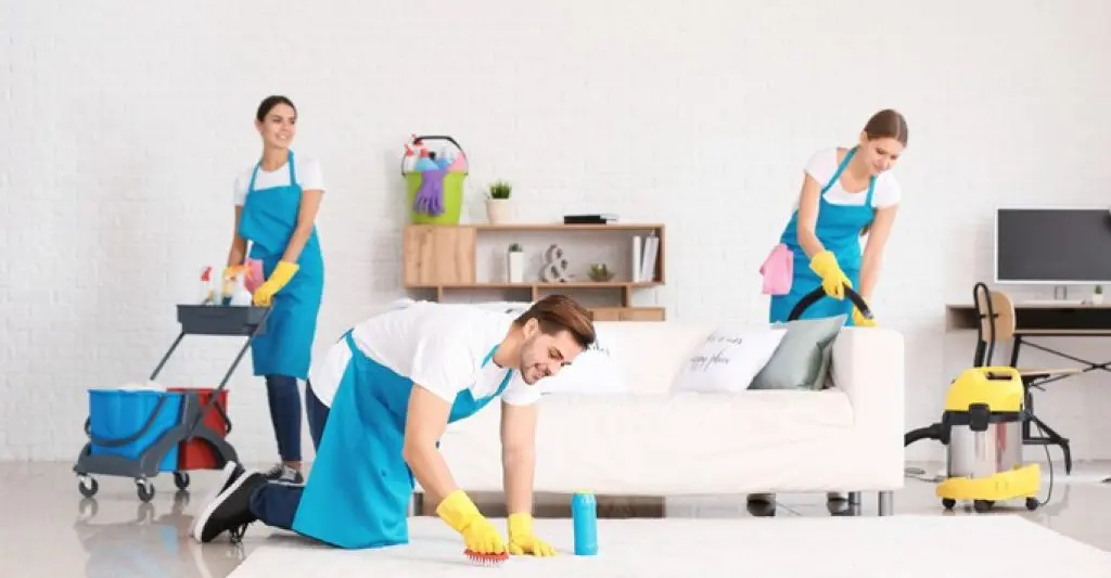 Team of professional cleaners in blue aprons cleaning a bright modern living room – representing top rated end of lease cleaning services by Dirt2Tidy.