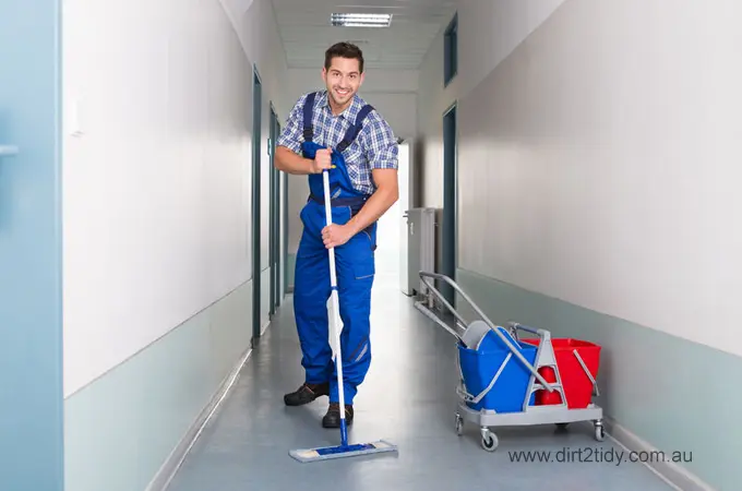 How Much does End of Lease Cleaning Cost for Brisbane? 5 Smiling male cleaner in blue uniform mopping a hallway with a bucket trolley – ideal for commercial and industrial cleaning services by Dirt2Tidy.