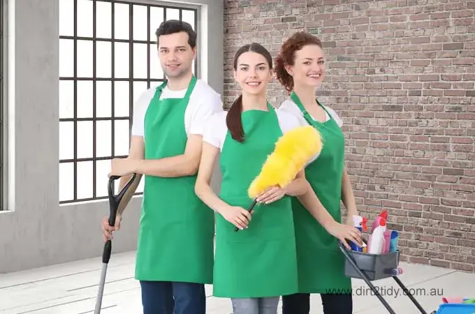Is there an end of lease cleaning service near me in Sydney? 2 Three professional cleaners in green aprons smiling and holding cleaning tools and a supply cart ā ready for residential or commercial cleaning service by Dirt2Tidy.