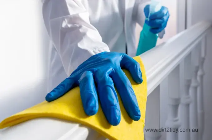 Person wearing gloves cleaning railing with spray and cloth.