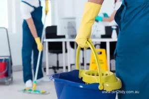 Close-up of a cleaner holding a mop bucket with others mopping floors in the background – representing efficient commercial or office cleaning services.