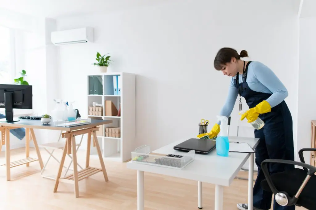 The DIY Guide to End Of Lease Cleaning 3 Cleaner disinfecting office desk with spray and gloves.