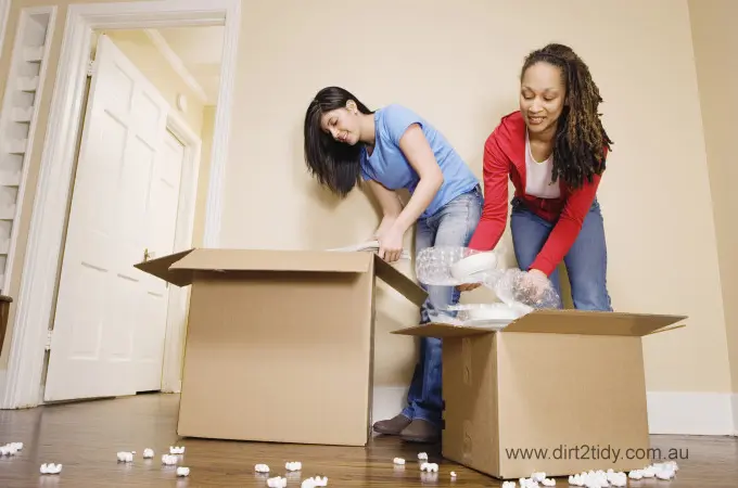 Two women unpacking their belongings after moving, preparing for end-of-lease cleaning.