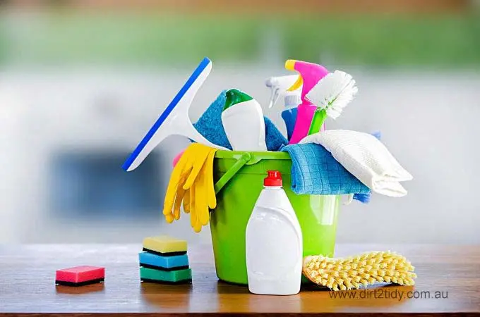  Assorted cleaning tools and sprays in a green bucket on a table.
