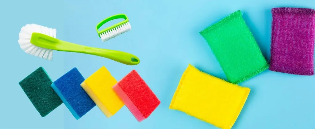 Various colorful sponges and scrub brushes arranged on a blue background for general cleaning tasks.