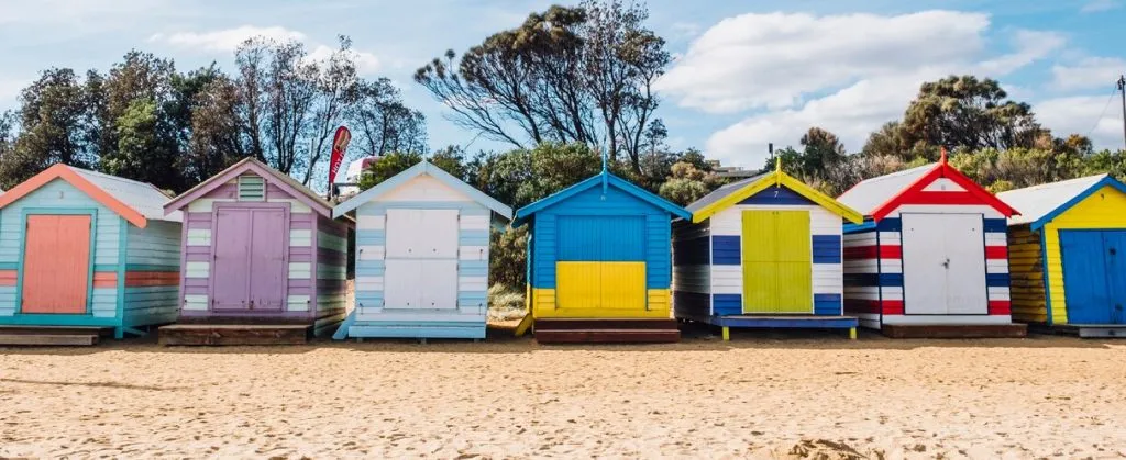 Suburb Guide: End of Lease Cleaning in Bondi 3 Row of colorful Brighton Beach bathing boxes on sandy shore with trees in the background.