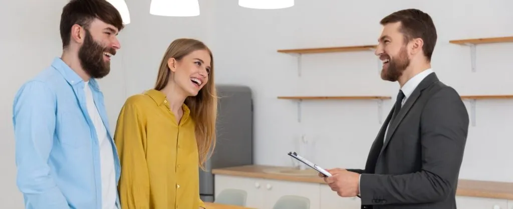 A cheerful couple smiling while speaking with a real estate agent inside a bright, empty rental property.