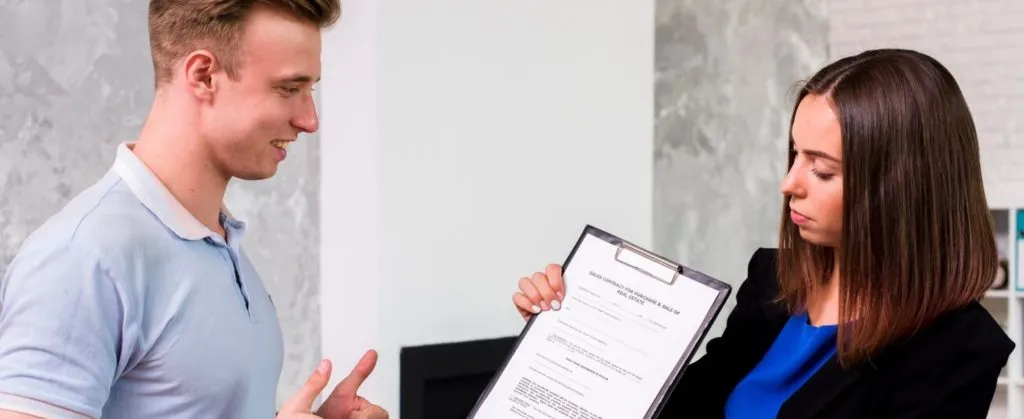 A young tenant listening as a property manager explains a rental inspection report on a clipboard.